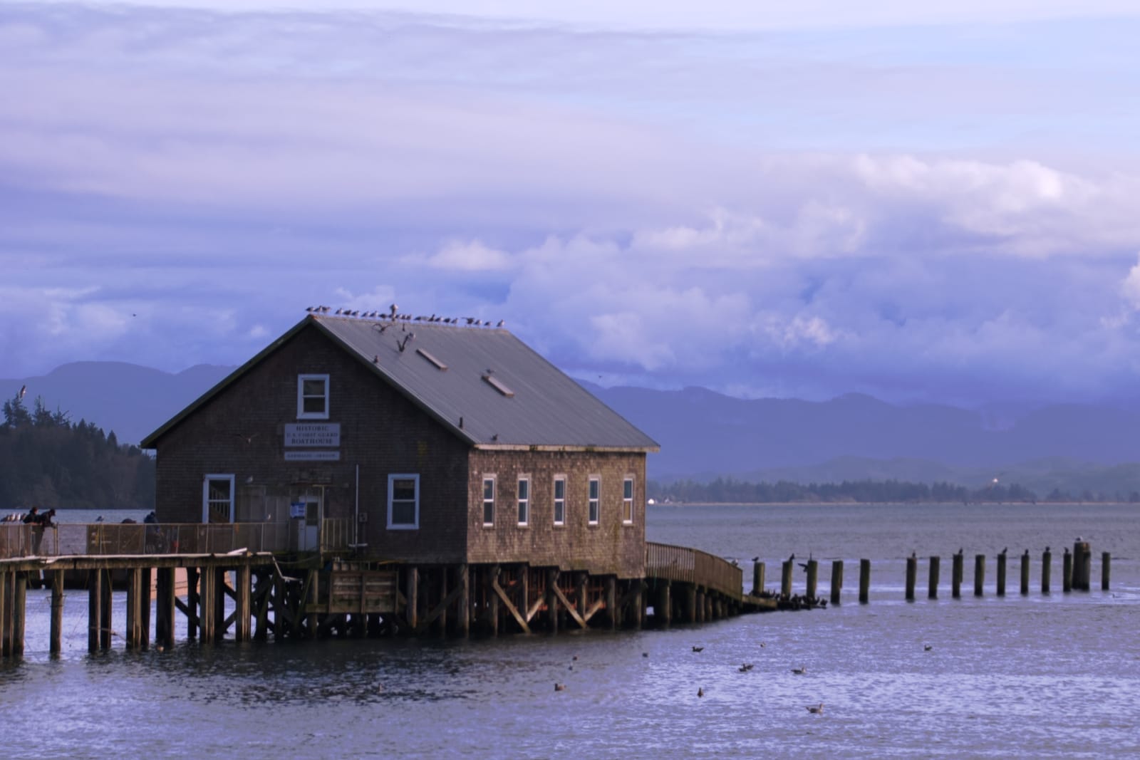 Weathered wooden pier building over Tillamook Bay under a cloudy sky